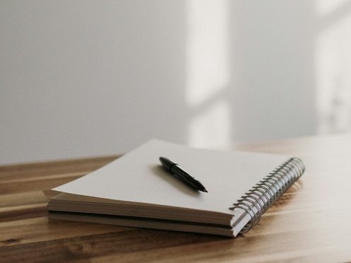 A closed notebook and pen on a wooden desk