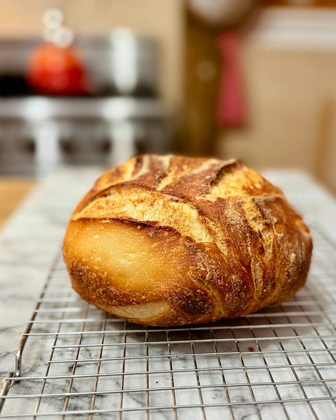 A scored sourdough loaf cooling on a wire rack