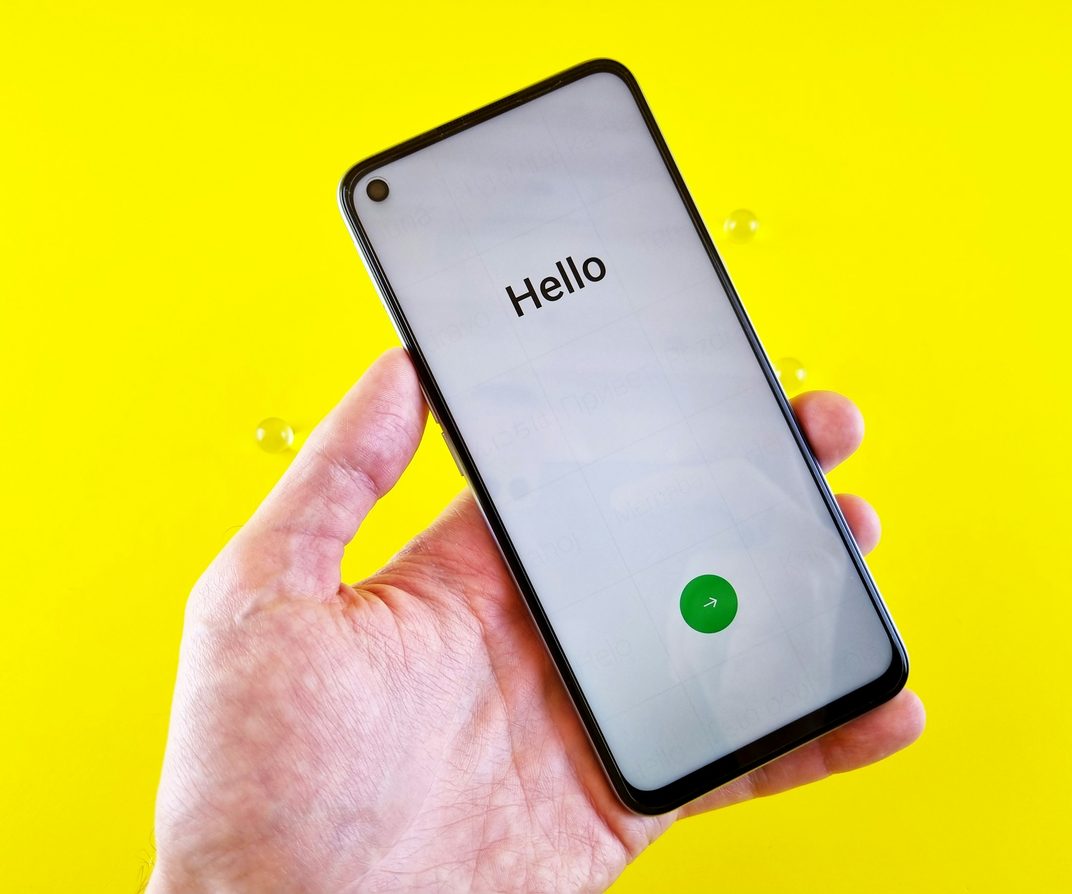 A hand holding up a phone against a bright yellow wall