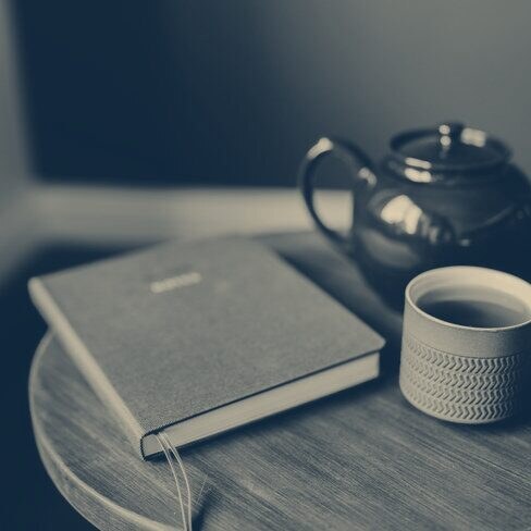 A closed book beside a cup of tea and a teapot