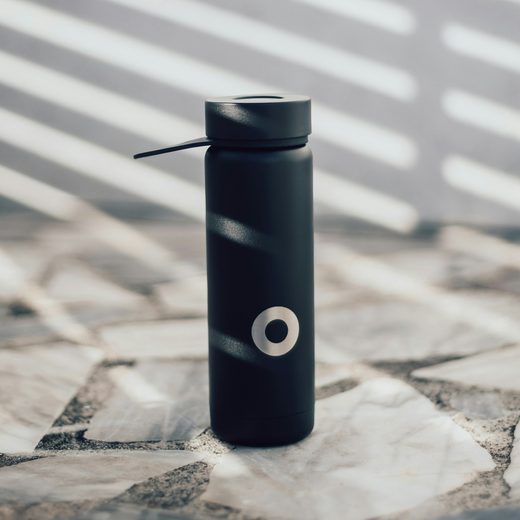 A matte black bottle with a carry loop standing on a stone patio