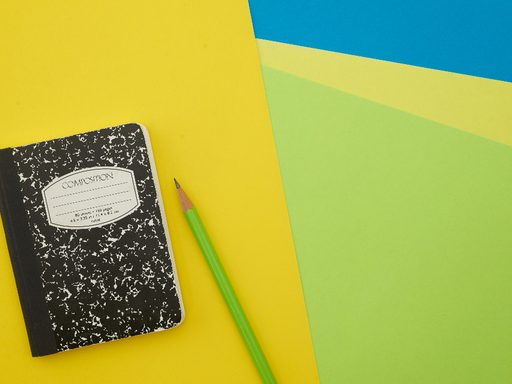 A composition notebook and a green pencil on yellow and green paper