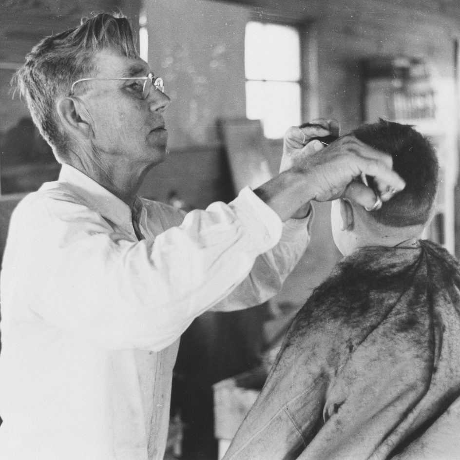 A barber trimming the back of a client's head in a black and white photograph