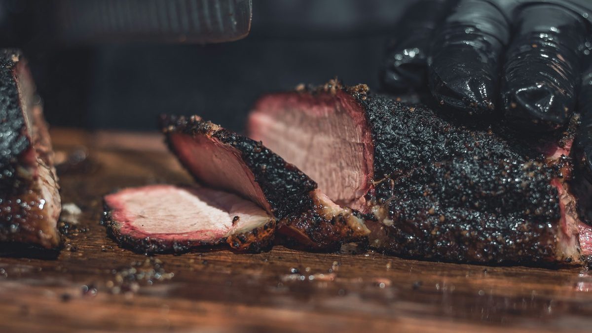 Smoked brisket with a dark bark, sliced on a wooden board
