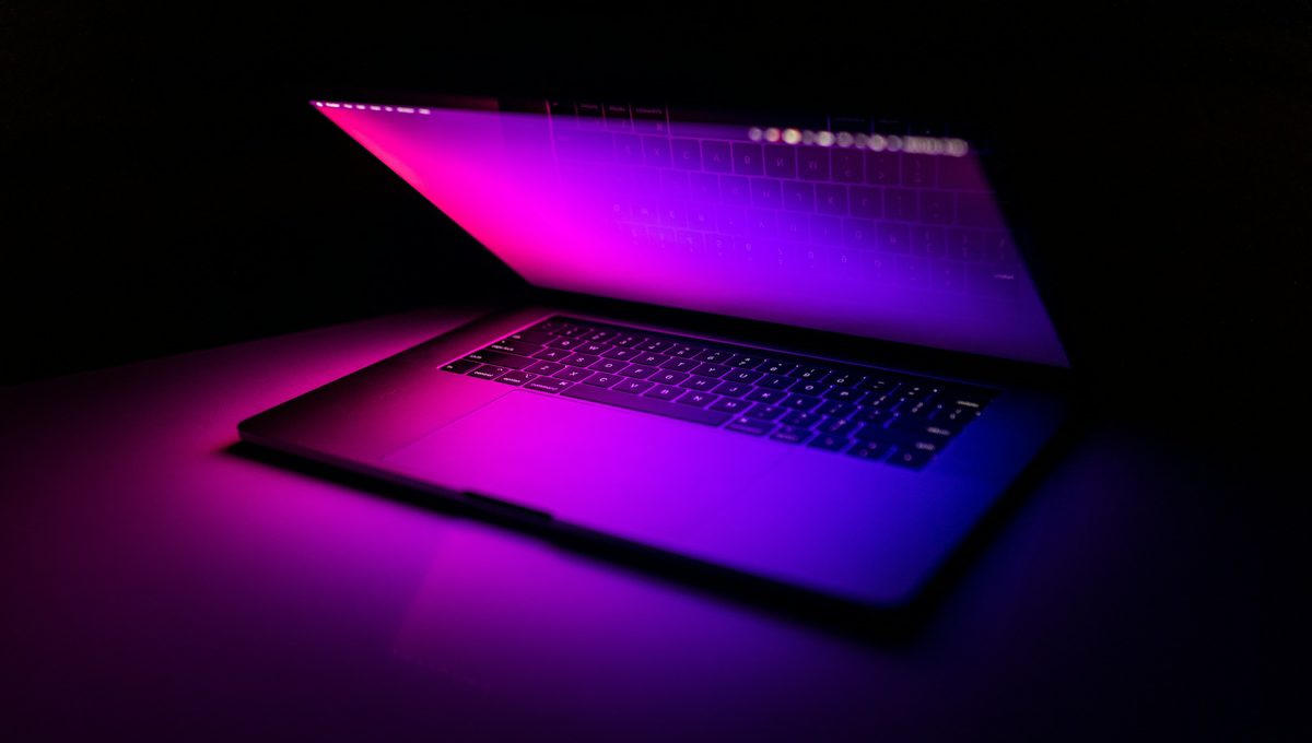 A laptop glowing magenta in a dark room