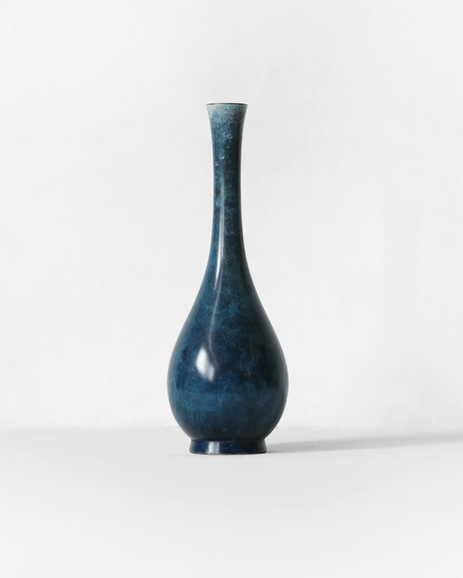 A slender blue ceramic vase on a white surface