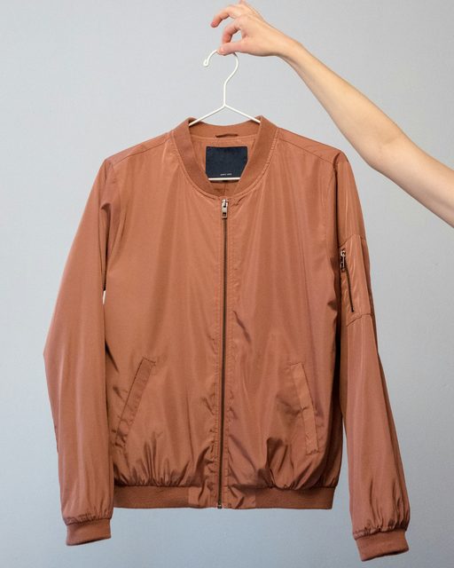 A rust bomber jacket held up on a hanger