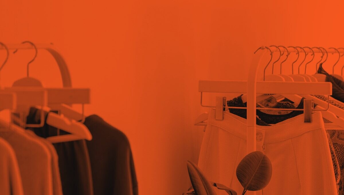 Clothing racks against a plain wall with a potted plant