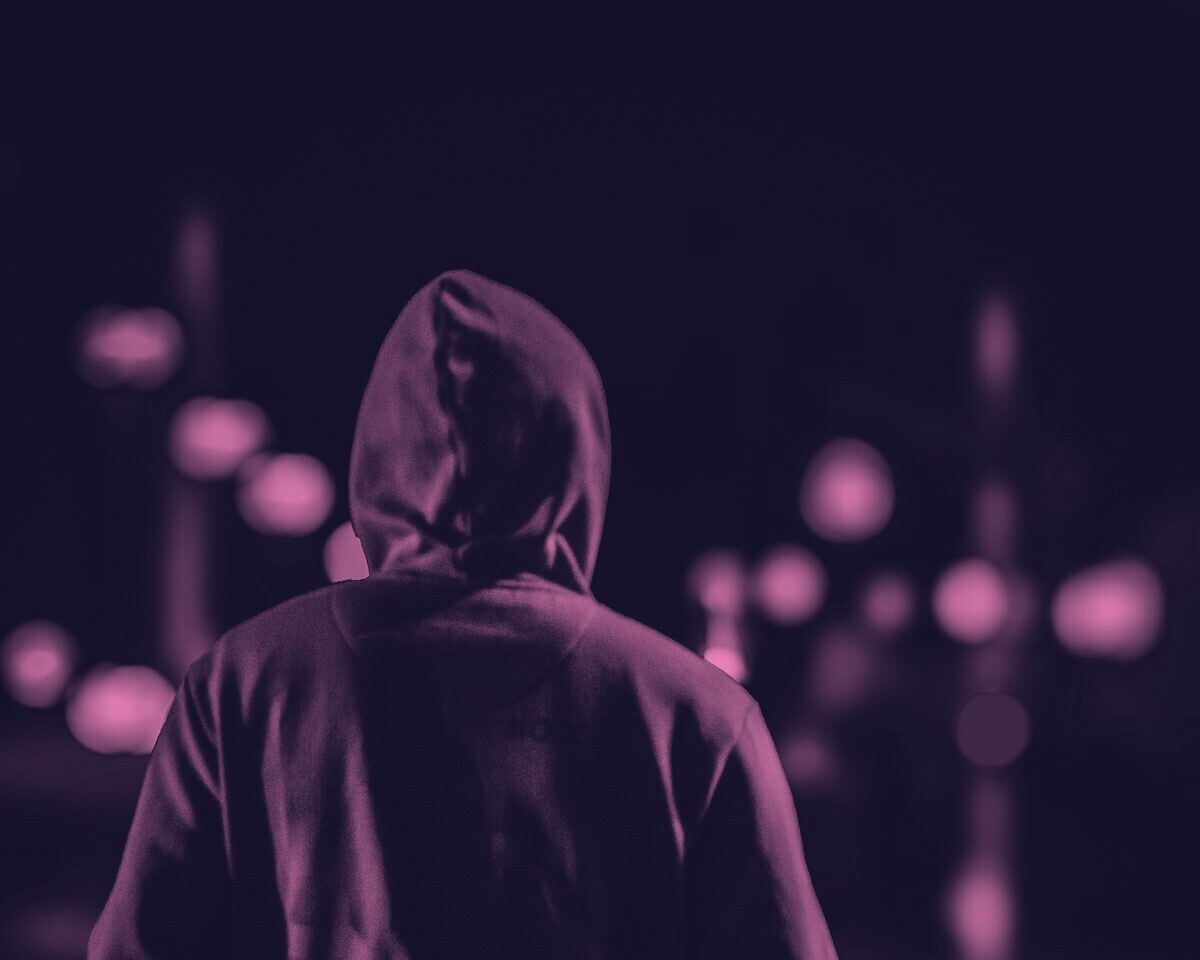 A person in a hoodie seen from behind on a city street at night