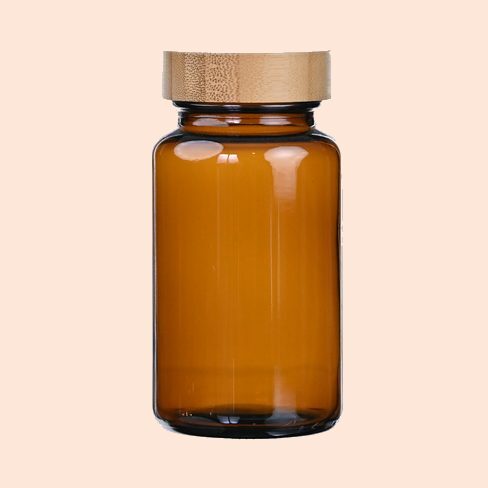 An amber glass bottle of facial oil with a wooden cap