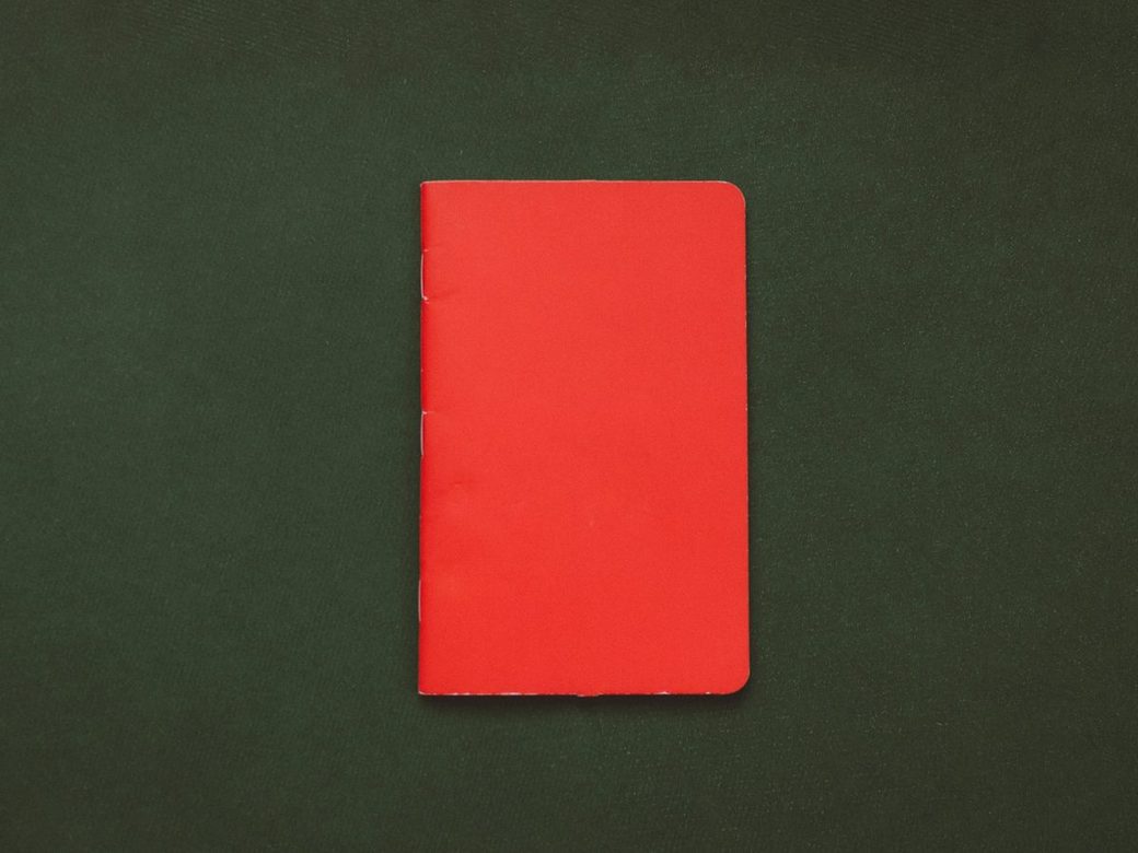 A plain red notebook lying on a dark green surface