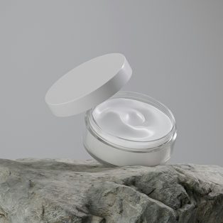 An open jar of white face cream on a gray stone