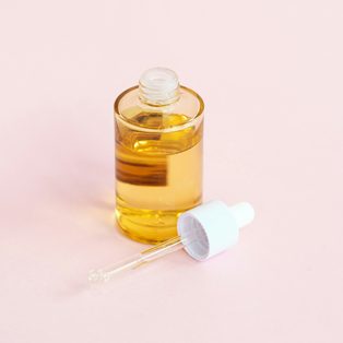 A glass dropper bottle of golden face oil on a pink ground