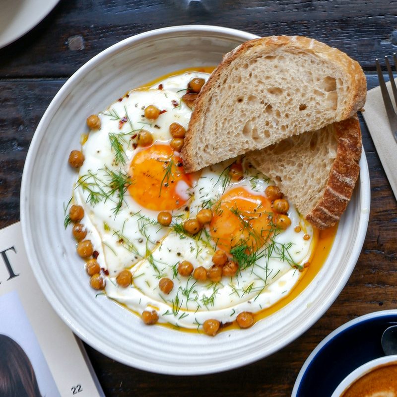 Fried eggs with crispy chickpeas and a slice of sourdough in a white bowl