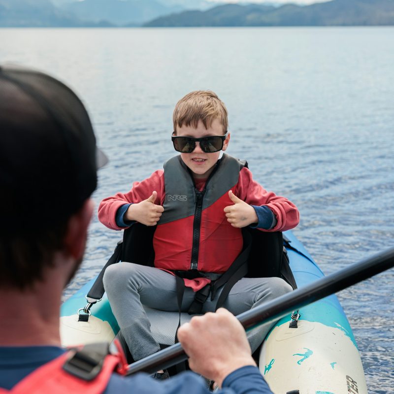 A boy in a life jacket giving two thumbs up from a canoe on a lake