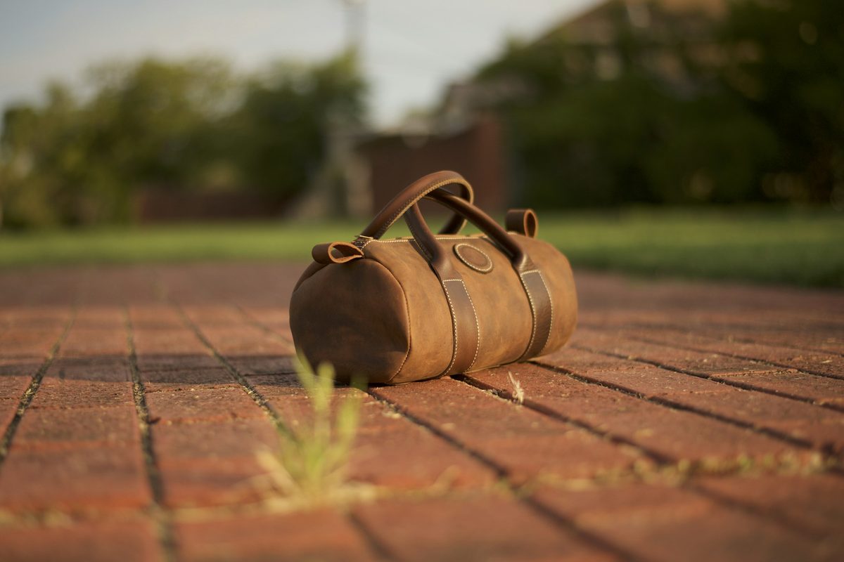 Tan leather weekender bag resting on a brick path in evening light