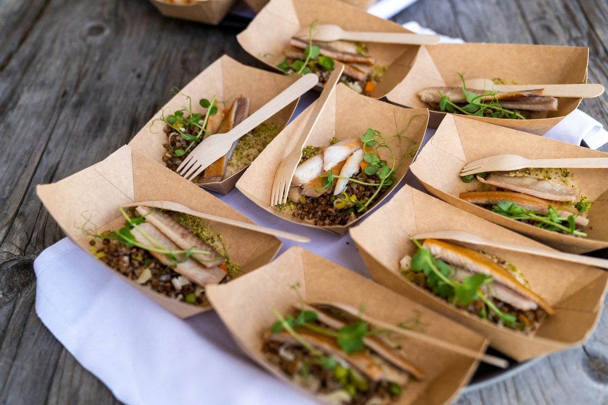 Individual kraft paper trays of fish, lentils and microgreens with wooden forks