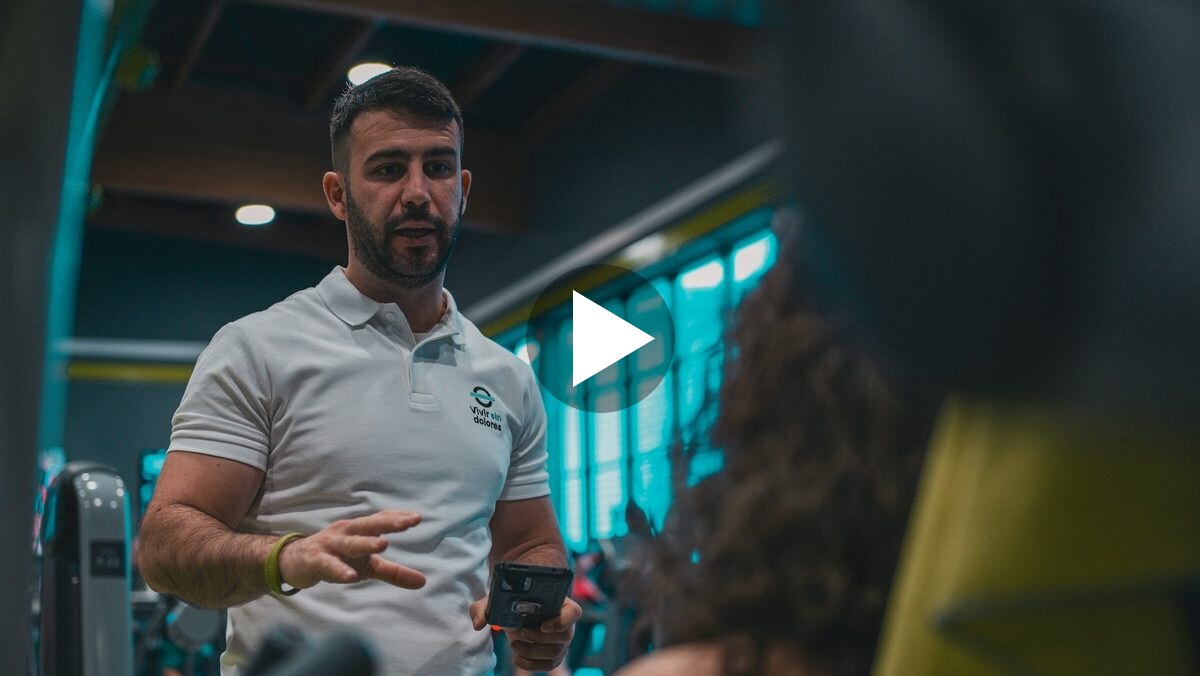 Coach in a gym talking to a client, with a play button over the frame