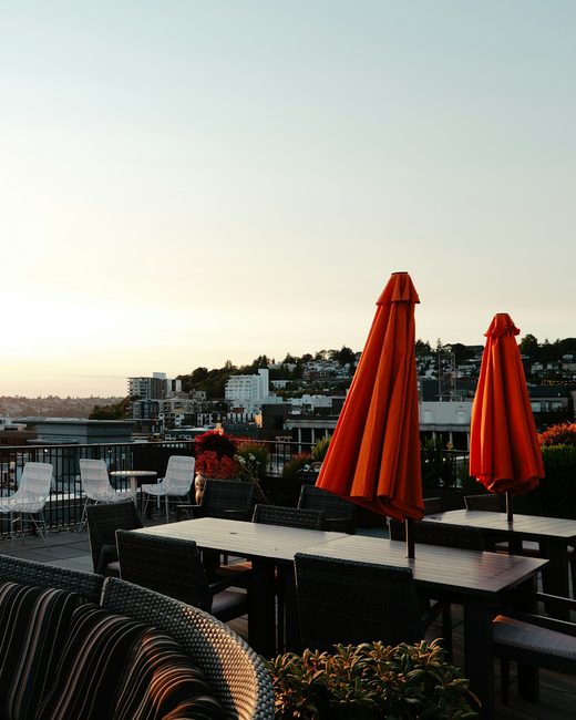 A rooftop terrace with red umbrellas over a bay at sunset