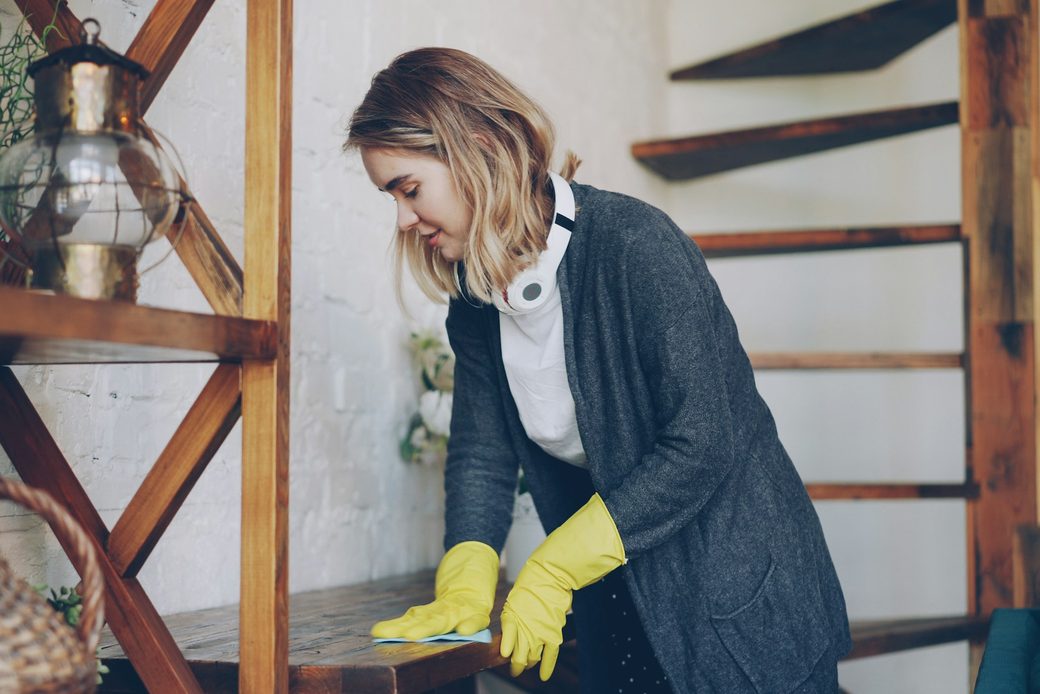 Cleaner in yellow gloves wiping down a wooden shelf