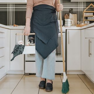 Cleaner in an apron sweeping a bright kitchen