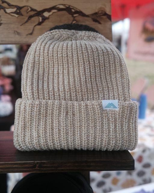 An oatmeal knit beanie on a wooden shelf