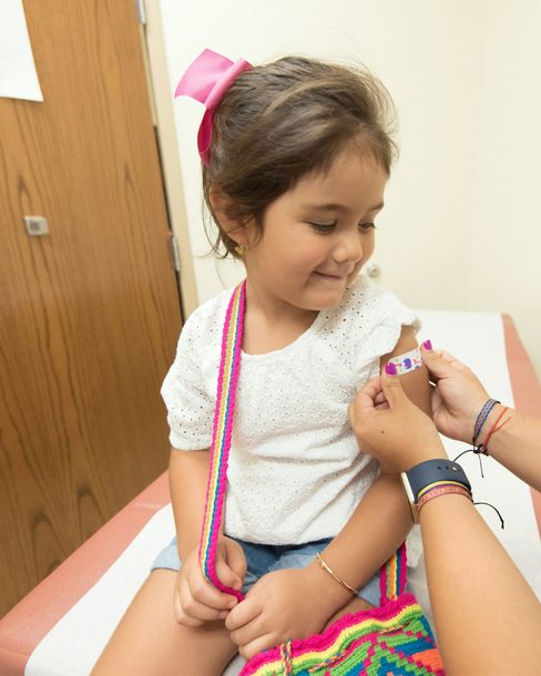 A smiling young girl getting a plaster on her arm after a shot