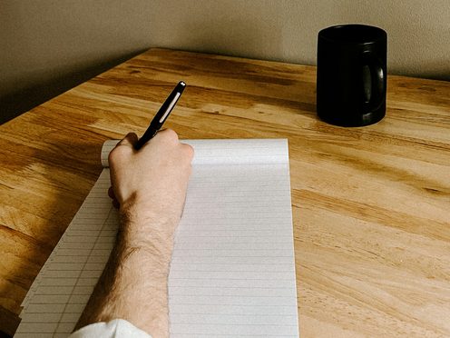 A hand writing notes on a pad at a wooden desk