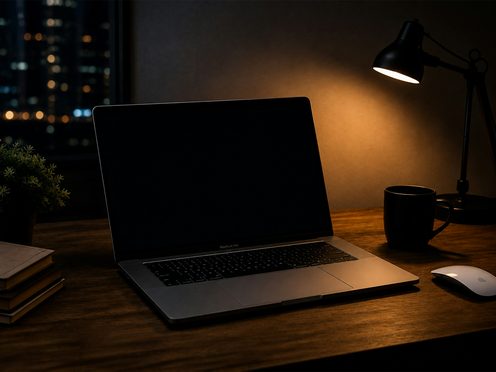 A laptop on a desk by a window at night, lit by a desk lamp