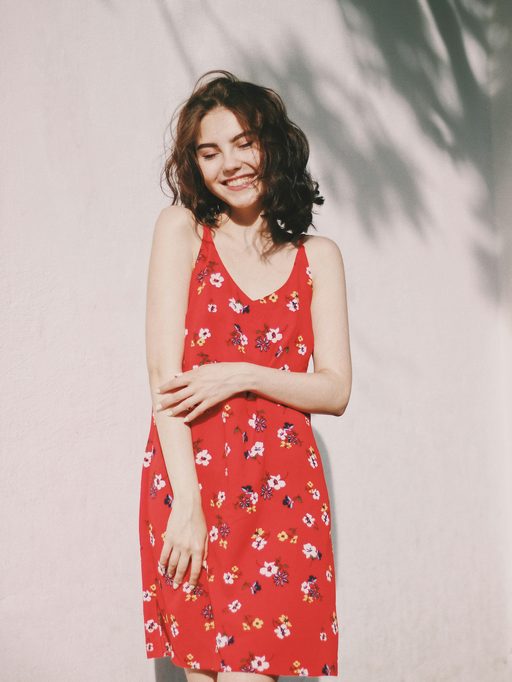 A woman in a red floral sundress laughing against a pale wall