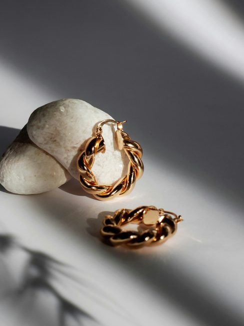 A pair of gold chain earrings beside a pebble
