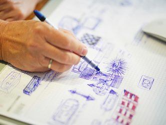 A hand sketching in blue pen across a page of drawings