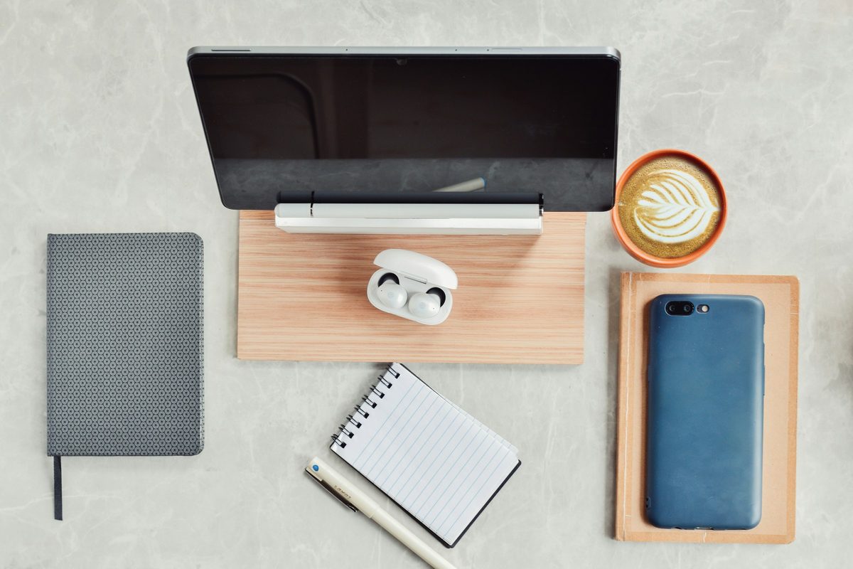 A tidy desk from above with a laptop, a notebook, a phone and a coffee