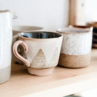 Speckled handmade mugs on a wooden shelf