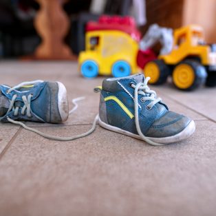 Small blue sneakers on the floor beside toy trucks