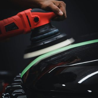 A rotary polisher working on the black paint of a car