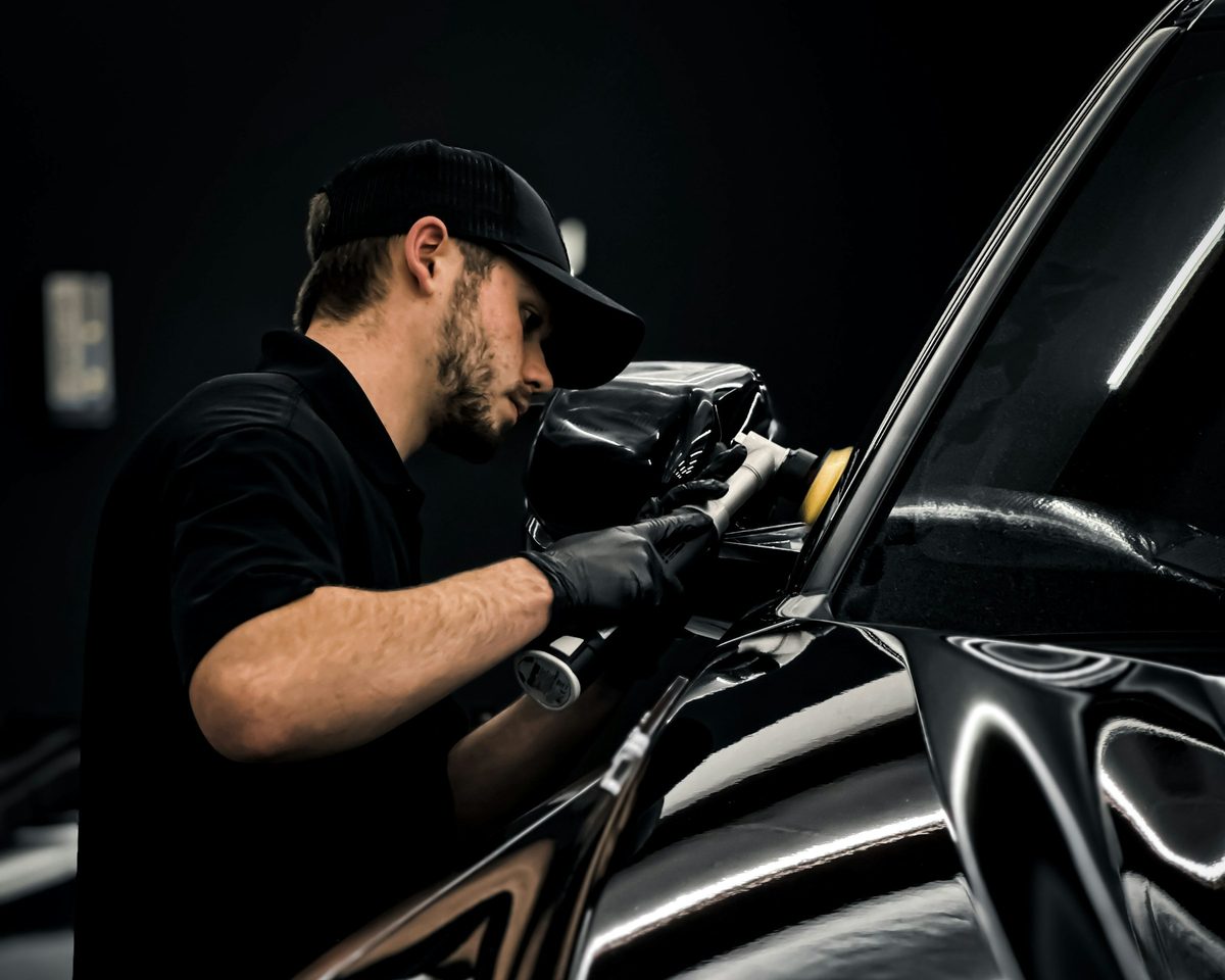 A detailer in black gloves machine-polishing the paint of a black car
