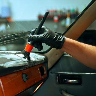 A gloved detailer brushing dust out of a car dashboard