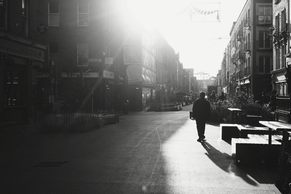 A figure walking across an empty city street at dawn, long shadows, in black and white