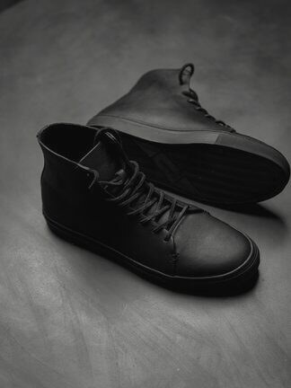 A pair of black leather high-top sneakers on a concrete floor