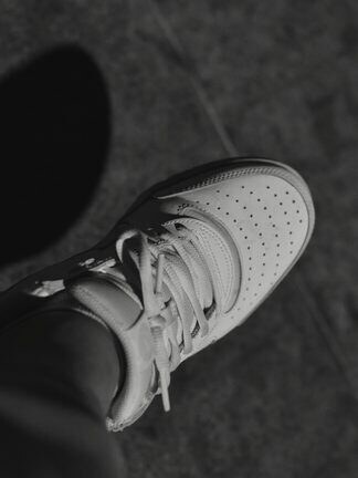 A white leather sneaker resting on a sidewalk in hard light