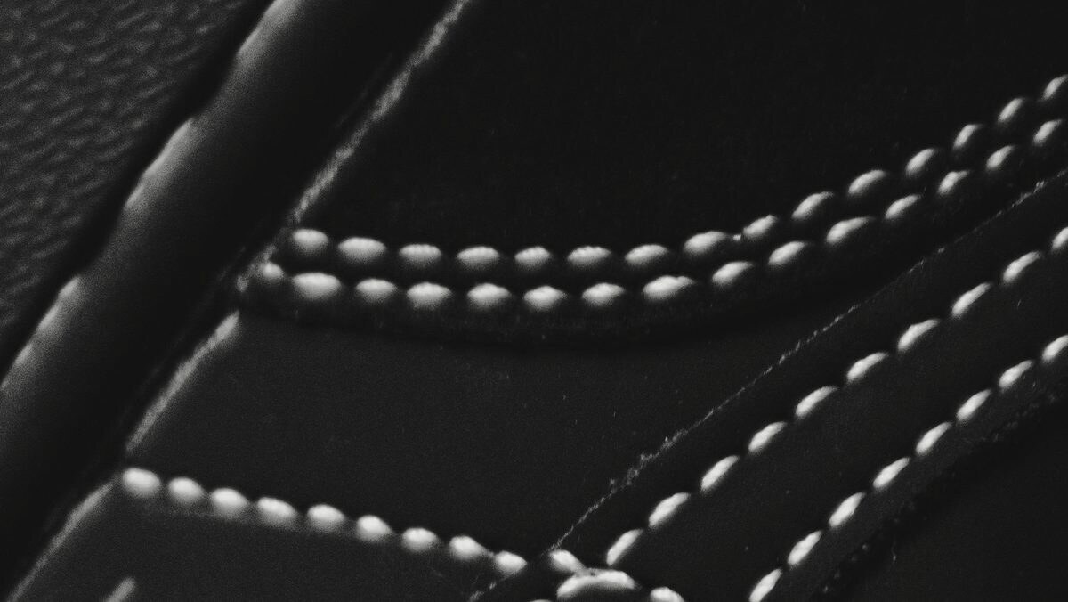 Close-up of white double stitching on a black leather sneaker upper