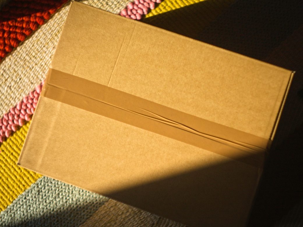 A cardboard box sealed with brown paper tape on a woven rug