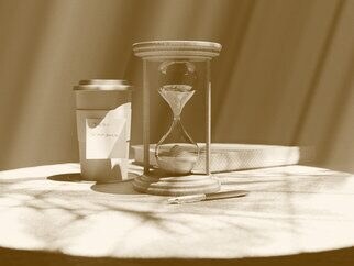 An hourglass on a table beside a cup