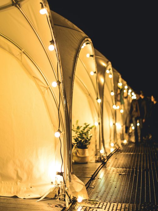 Festival tents glowing under string lights at dusk