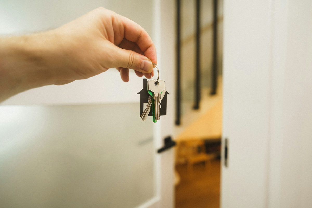 A hand holding a set of house keys beside an open front door