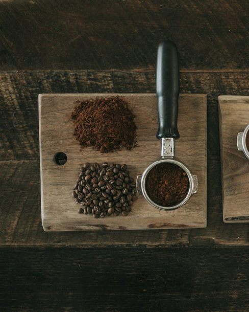 Whole beans, ground coffee and a latte on a wooden board