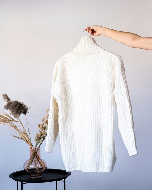 A cream ribbed knit sweater held up on a hanger