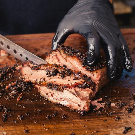 A gloved hand slicing smoked brisket on a cutting board