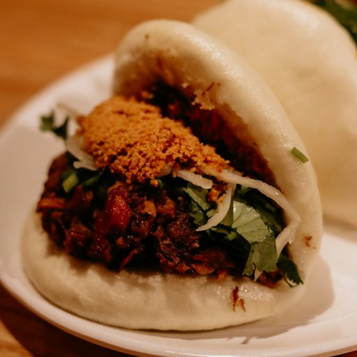 A steamed bao bun filled with braised pork and herbs